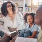 professora segurando livro didatico e ouvindo aluno
