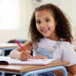 aluna em sala de aula escrevendo e sorrindo