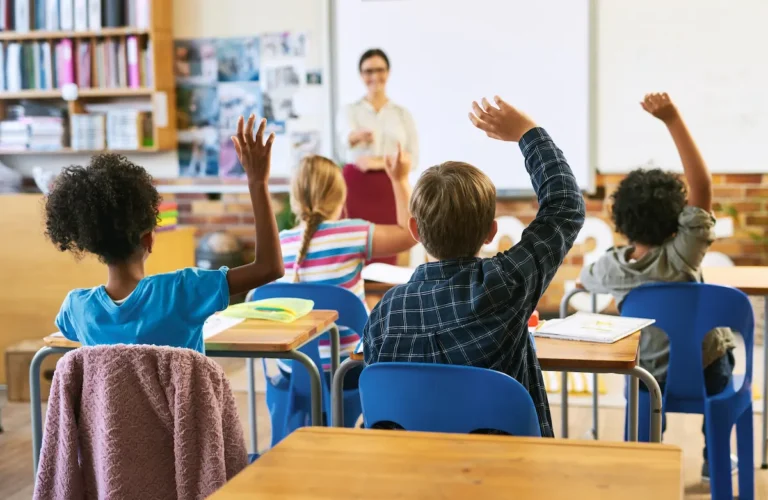 alunos em sala de aula levantando a mao para professora